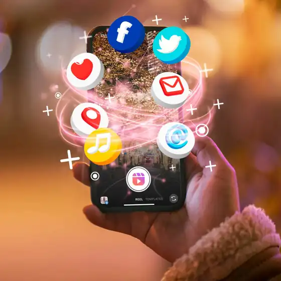 Hand holding a phone with Facebook, X, email, location, music and Reels icons floating above the screen
